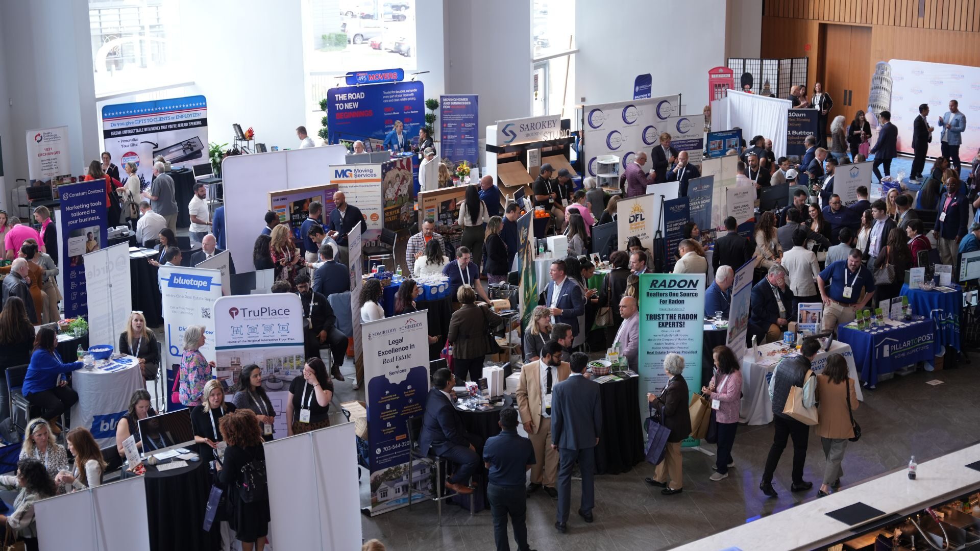 A bustling indoor convention with numerous people interacting at various information booths, showcasing different businesses and organizations in a spacious, well-lit hall.