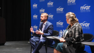 Two people are seated on stage at an event, engaging in discussion. The backdrop displays "NVAR Northern Virginia Association of Realtors."