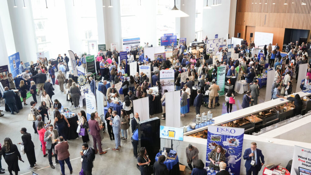 A bustling career fair with numerous booths and people networking in a spacious, well-lit indoor venue featuring large windows and modern design.