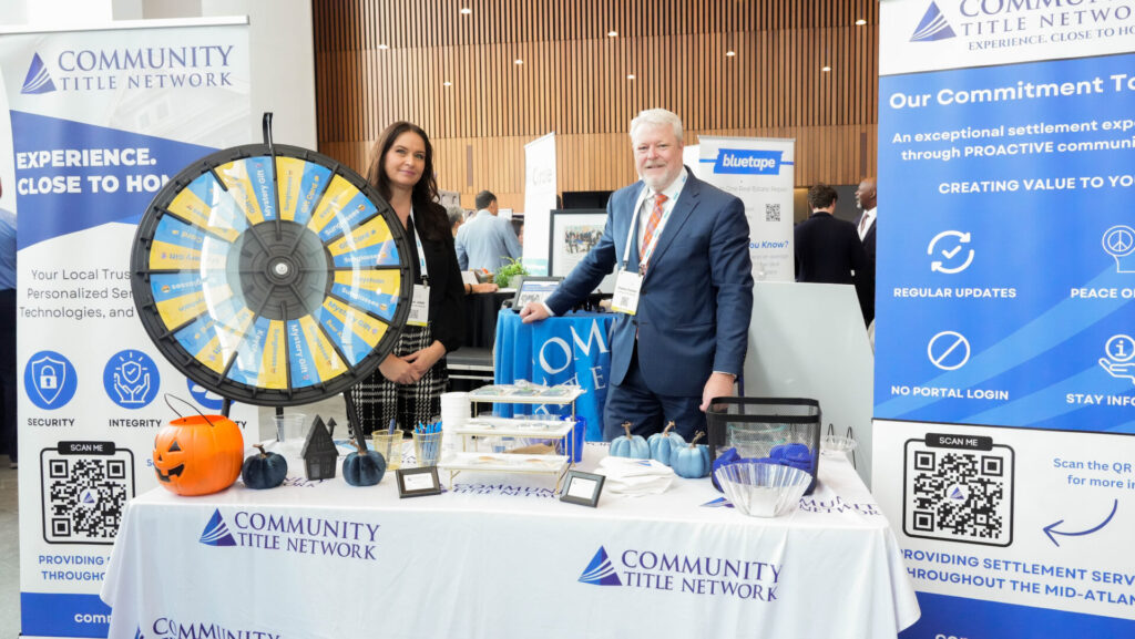 Two people stand at a booth with a prize wheel and promotional materials for "Community Title Network," featuring informational signs and decorations.