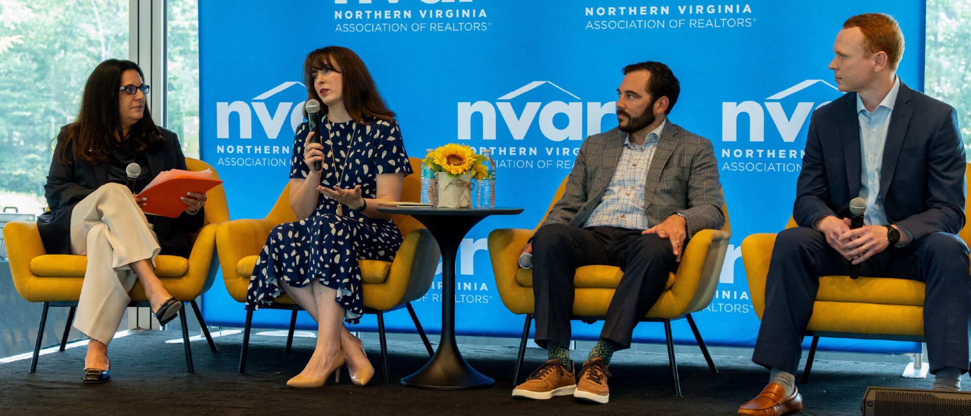 Four people are seated on stage, engaged in a panel discussion. A "Northern Virginia Association of Realtors" backdrop is visible behind them.