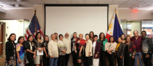 A group of people standing in front of a projector screen with U.S. and Philippine flags on either side.