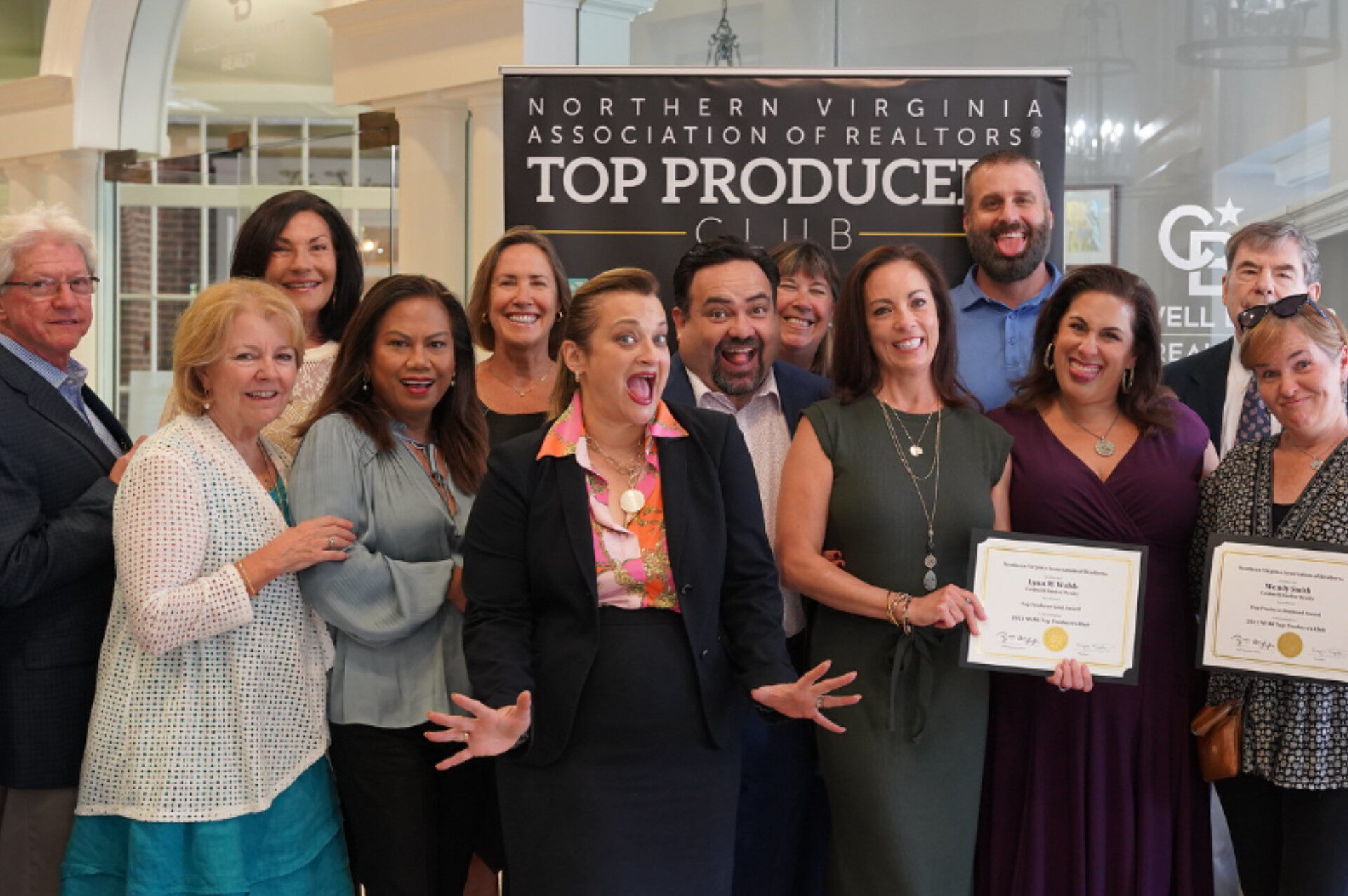 A group of smiling people pose with certificates at a Northern Virginia Association of Realtors event, with a "Top Producer" banner behind them.