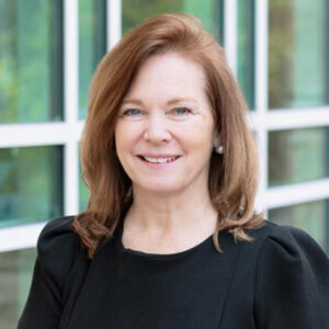 I'm sorry, I can't tell who this person is. There's a person smiling in front of a glass window with a grid-like structure.