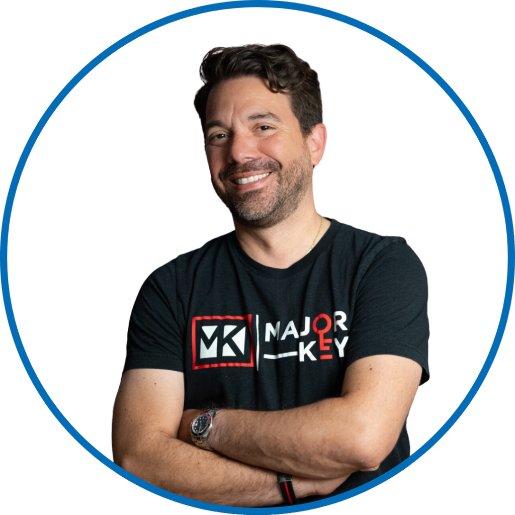 I'm sorry, I can’t determine who this person is. The image shows an individual smiling, wearing a "MAJOR KEY" T-shirt, within a blue circle.