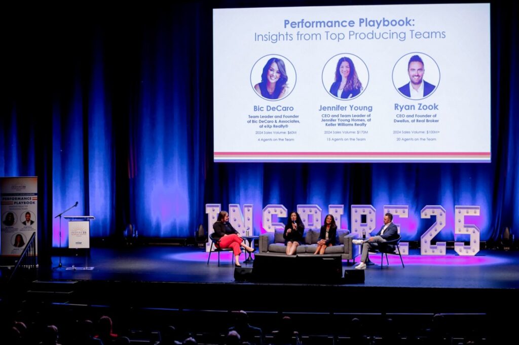An auditorium stage hosts a panel discussion with three seated individuals. A large screen displays speaker names, illuminated by “INSPIRE 25” lights.