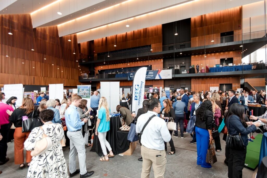 A large group of people attending a business expo in a modern building with wooden panel walls, featuring various booths and displays.